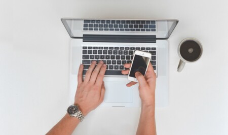 computer på bord og en med mobil i hånden